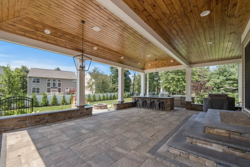 Spacious covered patio featuring a luxurious outdoor kitchen with stone countertops and built-in appliances, surrounded by lush landscaping.