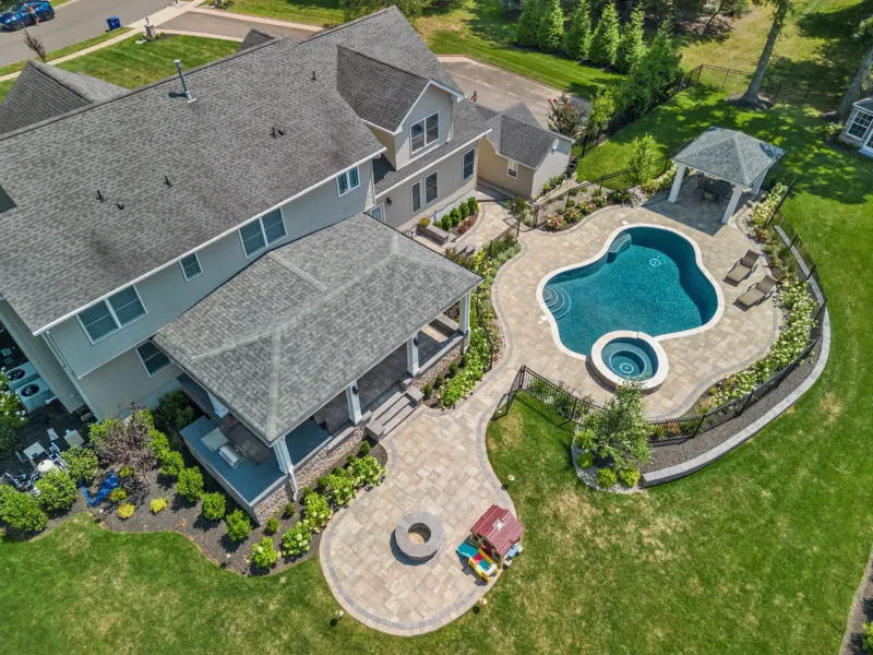 Professionally designed backyard with custom pool and paver patio, landscaping, and a covered paver patio, as viewed from above.