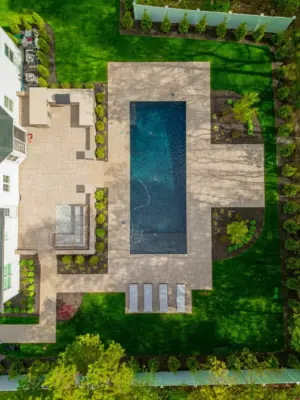 A full backyard transformation featuring a raised patio with stone retaining wall and pillars, paver pool patio with coping, paver steps with integrated LED lighting, a paver walkway with path lights, Japanese maple specimen plantings, arborvitae privacy screening, and sod installation.