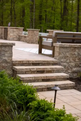 A full backyard transformation featuring a raised patio with stone retaining wall and pillars, paver pool patio with coping, paver steps with integrated LED lighting, a paver walkway with path lights, Japanese maple specimen plantings, arborvitae privacy screening, and sod installation.