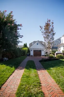 Scenic View Landscaping transformed a Spring Lake property with a complete front and backyard renovation, featuring beach-inspired landscaping, custom lighting, bluestone patio, brick driveway, outdoor kitchen, new sod, drainage, and concrete walkways.