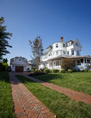 Scenic View Landscaping transformed a Spring Lake property with a complete front and backyard renovation, featuring beach-inspired landscaping, custom lighting, bluestone patio, brick driveway, outdoor kitchen, new sod, drainage, and concrete walkways.