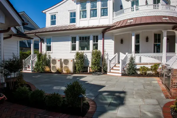 Scenic View Landscaping transformed a Spring Lake property with a complete front and backyard renovation, featuring beach-inspired landscaping, custom lighting, bluestone patio, brick driveway, outdoor kitchen, new sod, drainage, and concrete walkways.