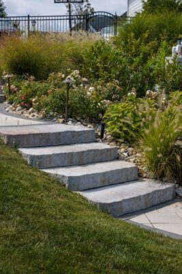 Scenic View Landscaping transformed a Lincroft, NJ property with a natural stone stairway, Techo-Bloc pool hardscaping, covered outdoor living area, and lush new landscaping.