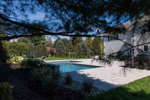 Scenic View Landscaping transformed a Colts Neck backyard into a modern outdoor oasis with Techo-Bloc pavers, Raffinato coping, triple waterfall spillways, outdoor kitchen, and custom lighting.