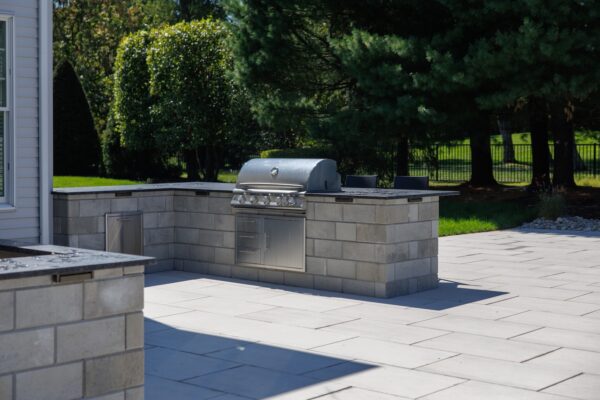 Scenic View Landscaping transformed a Colts Neck backyard into a modern outdoor oasis with Techo-Bloc pavers, Raffinato coping, triple waterfall spillways, outdoor kitchen, and custom lighting.