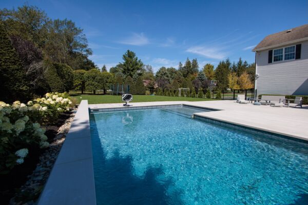Scenic View Landscaping transformed a Colts Neck backyard into a modern outdoor oasis with Techo-Bloc pavers, Raffinato coping, triple waterfall spillways, outdoor kitchen, and custom lighting.