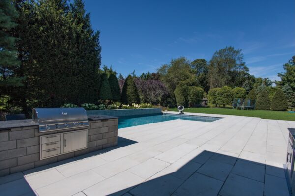 Scenic View Landscaping transformed a Colts Neck backyard into a modern outdoor oasis with Techo-Bloc pavers, Raffinato coping, triple waterfall spillways, outdoor kitchen, and custom lighting.