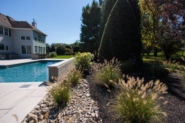 Scenic View Landscaping transformed a Colts Neck backyard into a modern outdoor oasis with Techo-Bloc pavers, Raffinato coping, triple waterfall spillways, outdoor kitchen, and custom lighting.