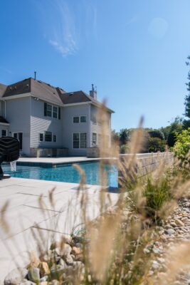 Scenic View Landscaping transformed a Colts Neck backyard into a modern outdoor oasis with Techo-Bloc pavers, Raffinato coping, triple waterfall spillways, outdoor kitchen, and custom lighting.