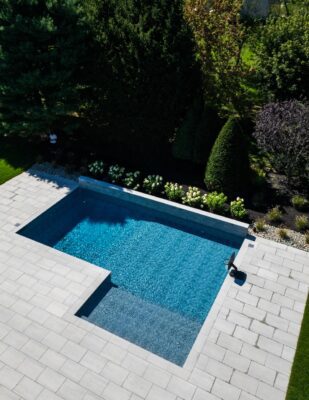 Scenic View Landscaping transformed a Colts Neck backyard into a modern outdoor oasis with Techo-Bloc pavers, Raffinato coping, triple waterfall spillways, outdoor kitchen, and custom lighting.
