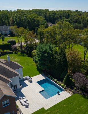 Scenic View Landscaping transformed a Colts Neck backyard into a modern outdoor oasis with Techo-Bloc pavers, Raffinato coping, triple waterfall spillways, outdoor kitchen, and custom lighting.