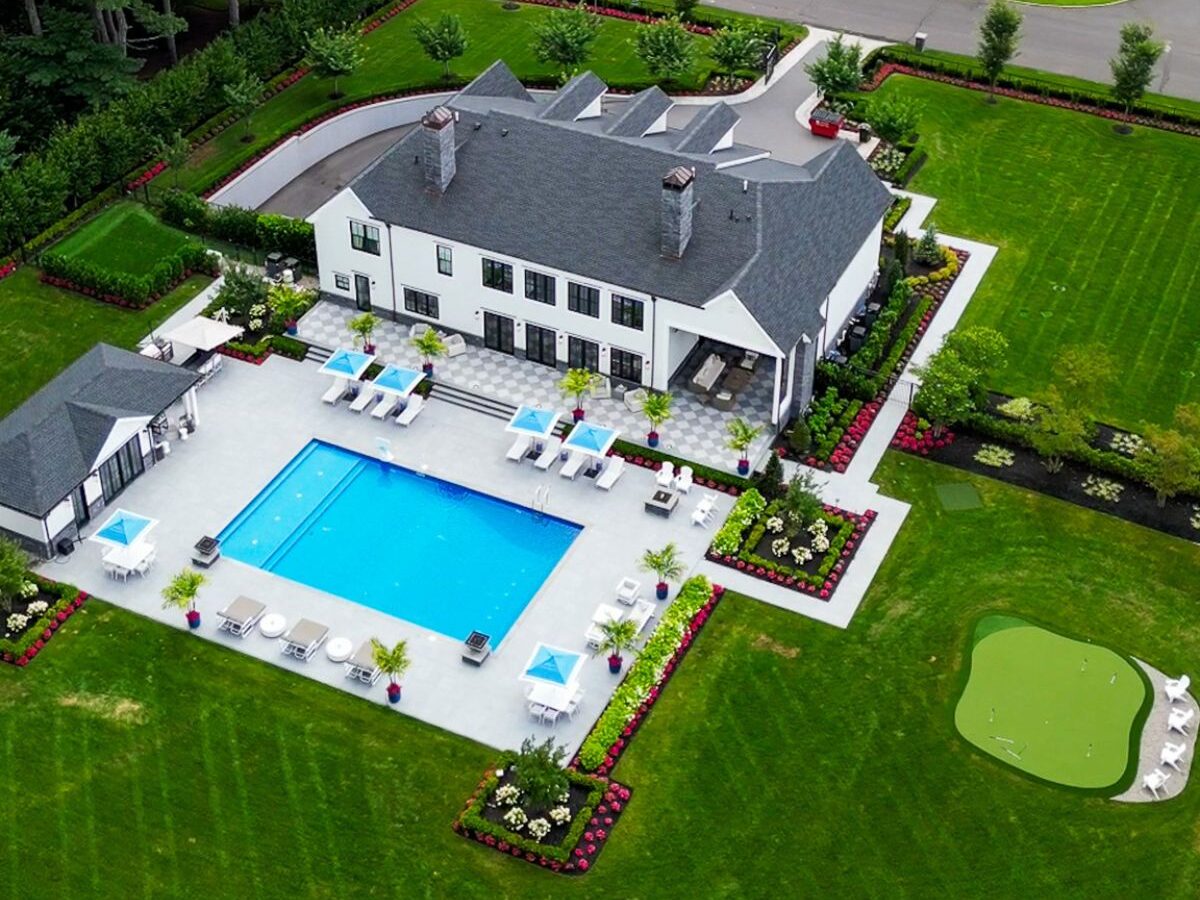 Aerial view of a custom backyard with inground pool, patio lounge area, landscape beds, and putting green in Colts Neck, NJ.