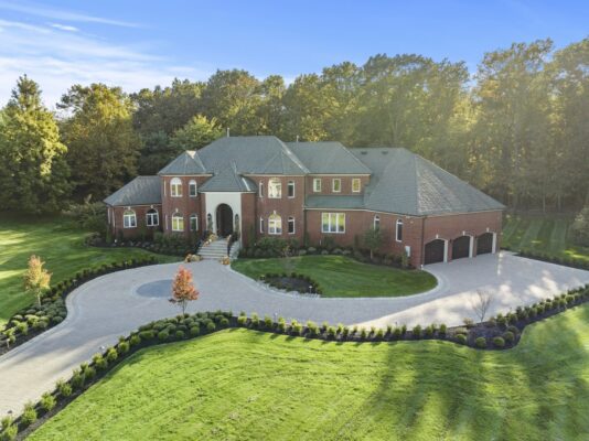 Wide aerial view of a custom brick paver driveway with circular inlay, front entrance steps, and landscaped front yard in Colts Neck NJ