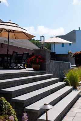Multi-level patio design in Colts Neck, NJ featuring a pool patio, retaining wall with steps, and raised patio with built-in lighting.