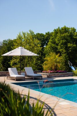 Complete outdoor transformation in Lincroft, NJ featuring a custom pool patio, fire pit patio with seating wall, stone steps, and a paver walkway connecting the backyard to the front.