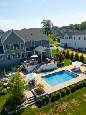 Complete outdoor transformation in Lincroft, NJ featuring a custom pool patio, fire pit patio with seating wall, stone steps, and a paver walkway connecting the backyard to the front.