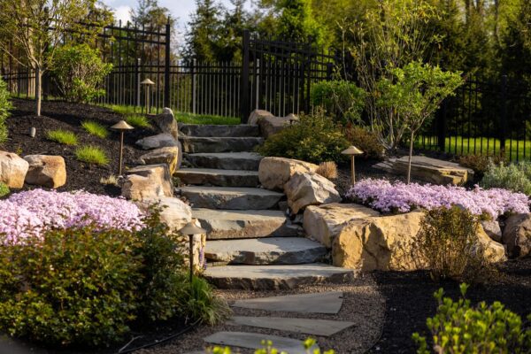 Two-level pool patio in Middletown, NJ featuring a stone retaining wall, natural stone steps, and a paver walkway connecting the backyard to the front yard.