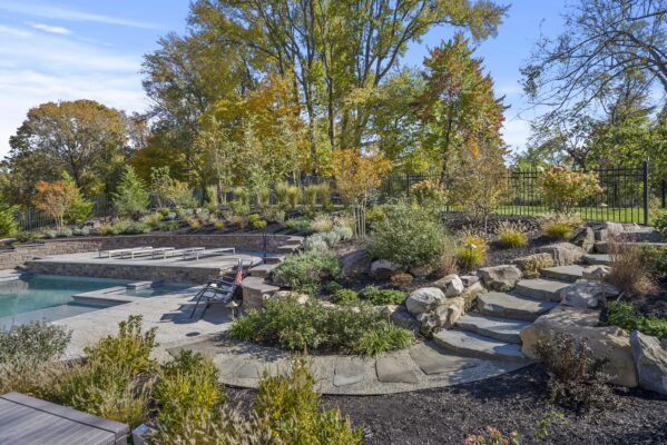 Two-level pool patio in Middletown, NJ featuring a stone retaining wall, natural stone steps, and a paver walkway connecting the backyard to the front yard.