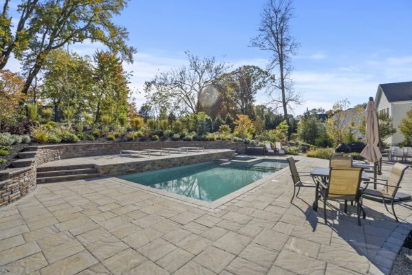 Two-level pool patio in Middletown, NJ featuring a stone retaining wall, natural stone steps, and a paver walkway connecting the backyard to the front yard.
