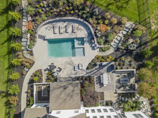 Two-level pool patio in Middletown, NJ featuring a stone retaining wall, natural stone steps, and a paver walkway connecting the backyard to the front yard.