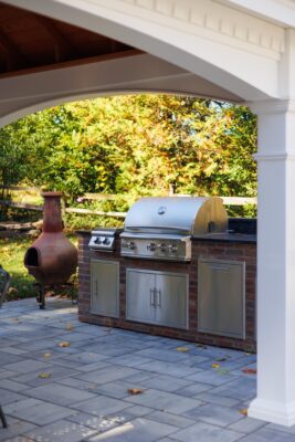 Outdoor living project in Rumson, NJ featuring a covered paver patio, outdoor kitchen, stone steps, natural stone walkway, and fire pit area.
