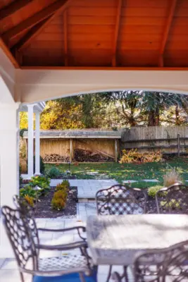 A covered paver patio with built-in outdoor kitchen, stone steps, natural stone walkway, and a dedicated fire pit area tied together with plantings and landscape lighting.