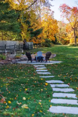 A covered paver patio with built-in outdoor kitchen, stone steps, natural stone walkway, and a dedicated fire pit area tied together with plantings and landscape lighting.