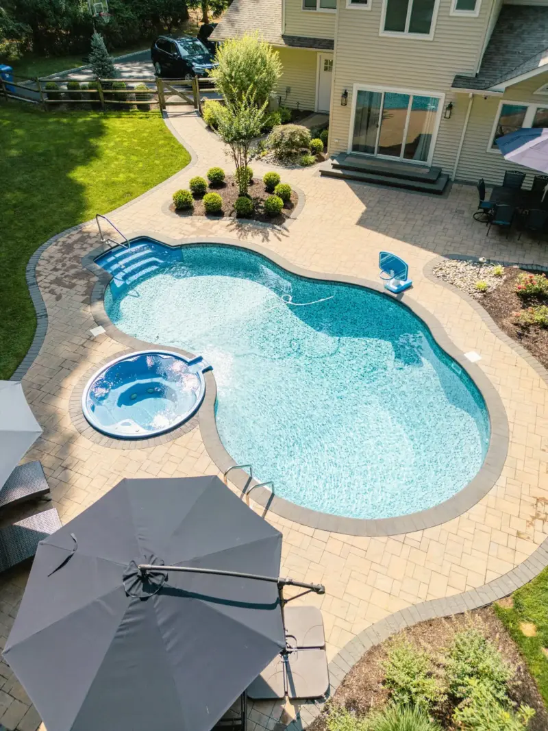 Aerial view of freeform pool and raised spa with paver pool patio, contrasting paver border, planting island and curved walkway to gate in Middletown, NJ