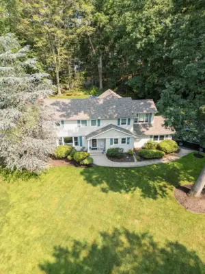 A paver pool patio wrapping a freeform pool and spa, a separate circular fire pit patio with built-in stone fire pit, a curved paver walkway, and refreshed planting beds on a wooded lot.