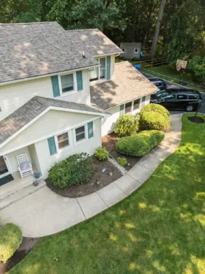 A paver pool patio wrapping a freeform pool and spa, a separate circular fire pit patio with built-in stone fire pit, a curved paver walkway, and refreshed planting beds on a wooded lot.